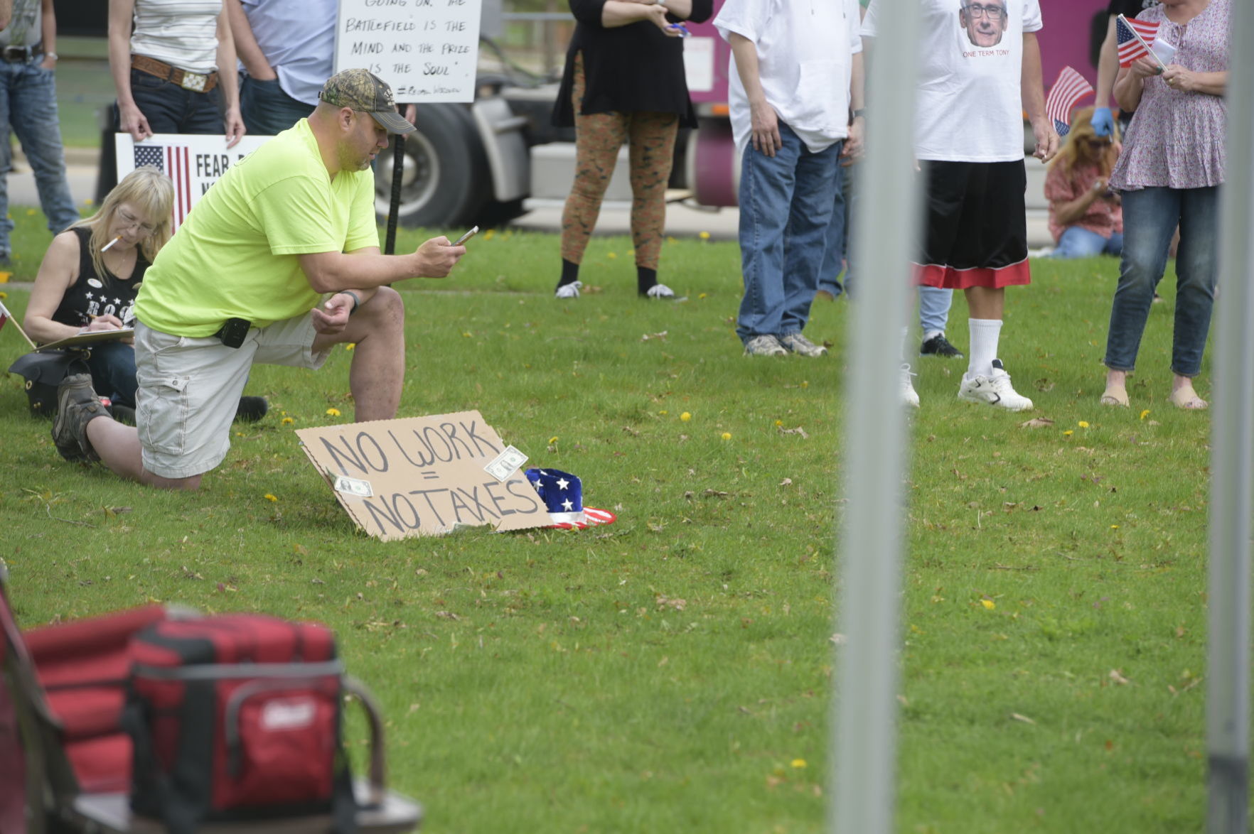 A man kneels next to his "No Work=No Taxes" sign